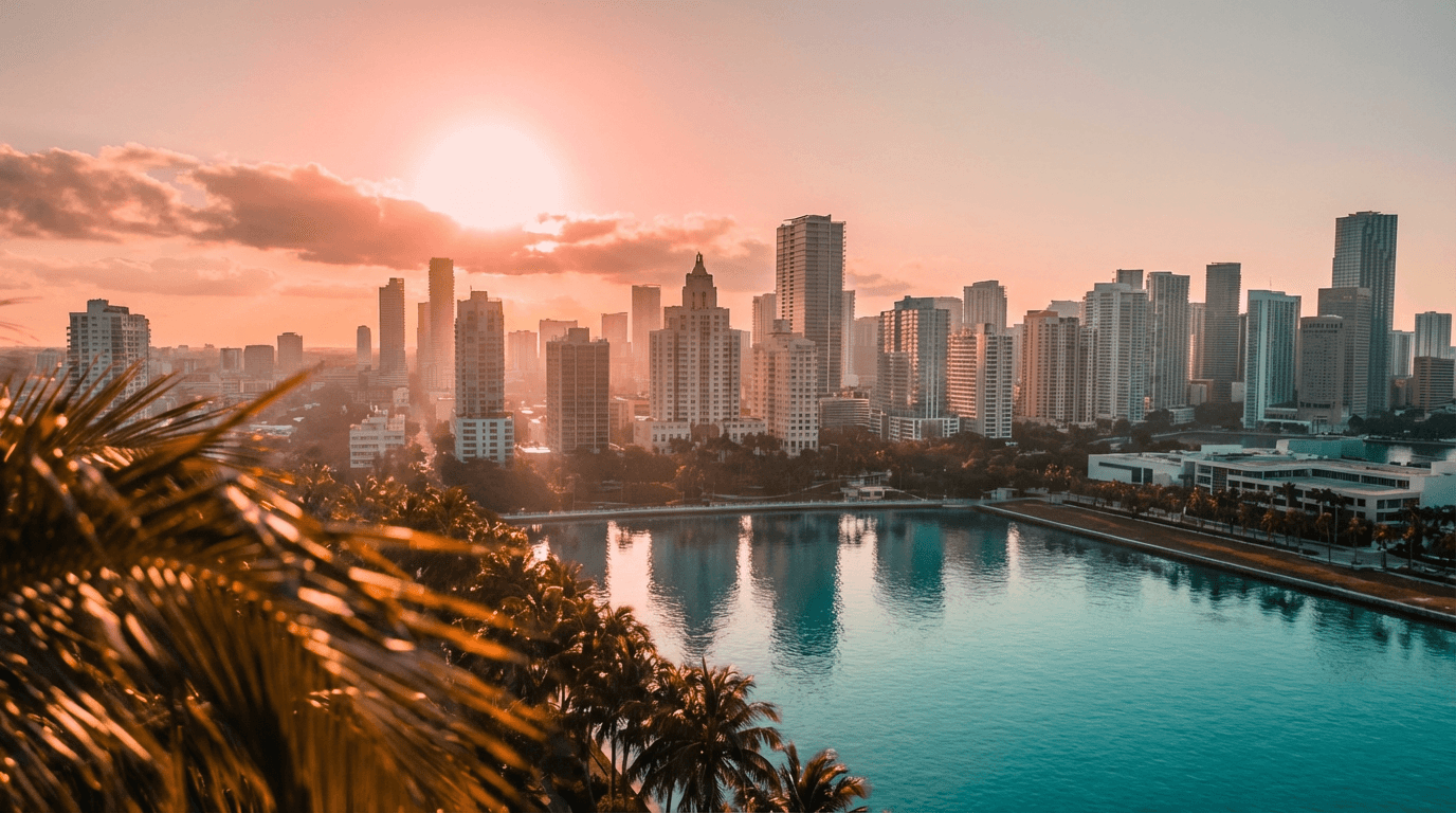Golden hour view of Miami skyline with palm fronds in foreground, reflecting in calm turquoise bay water.